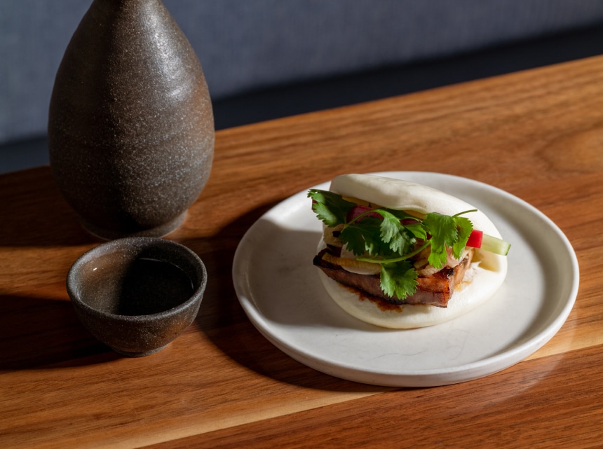 Tiger Cry Bao served on a white plate next to sake in a tokkuri.