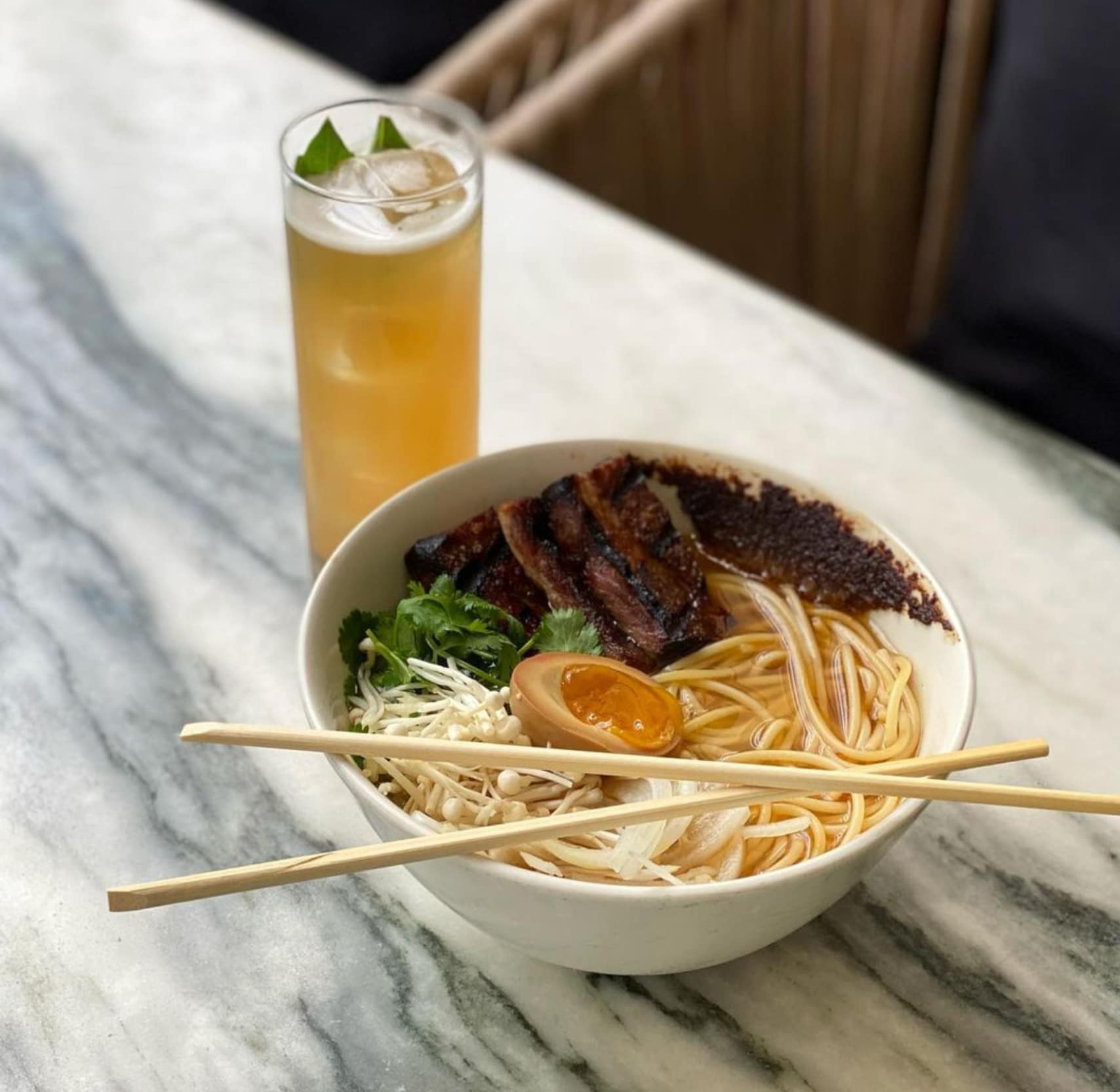 A bowl of uncommon ramen next to a cocktail.