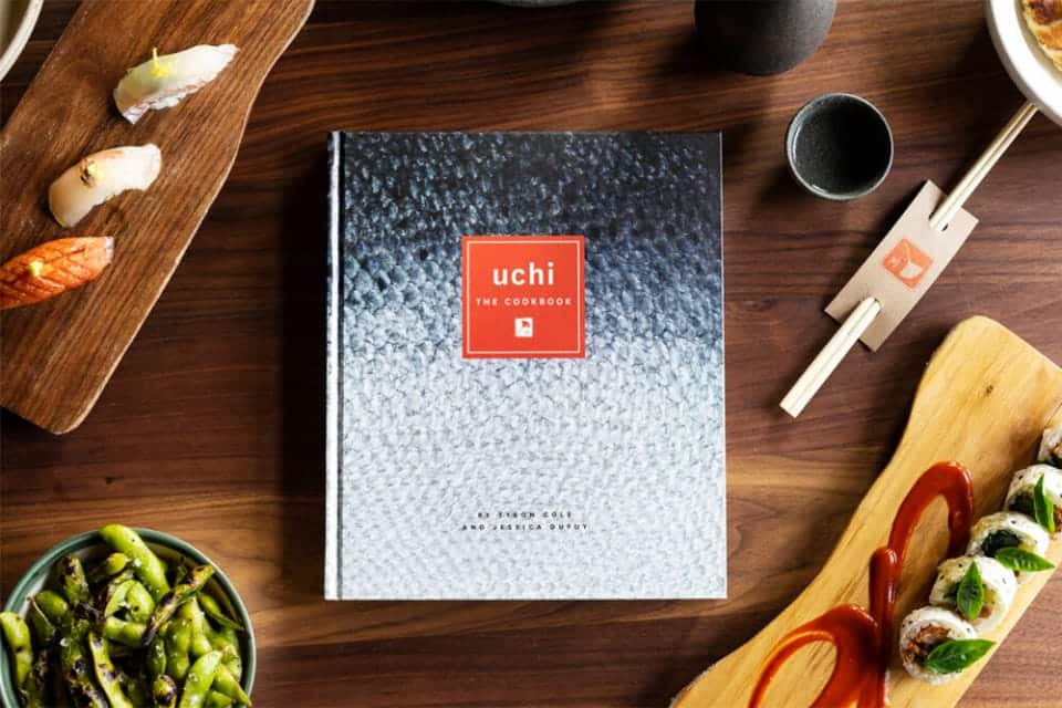 The Uchi Cookbook placed on a table surrounded by prepared food and a pair of chopsticks.