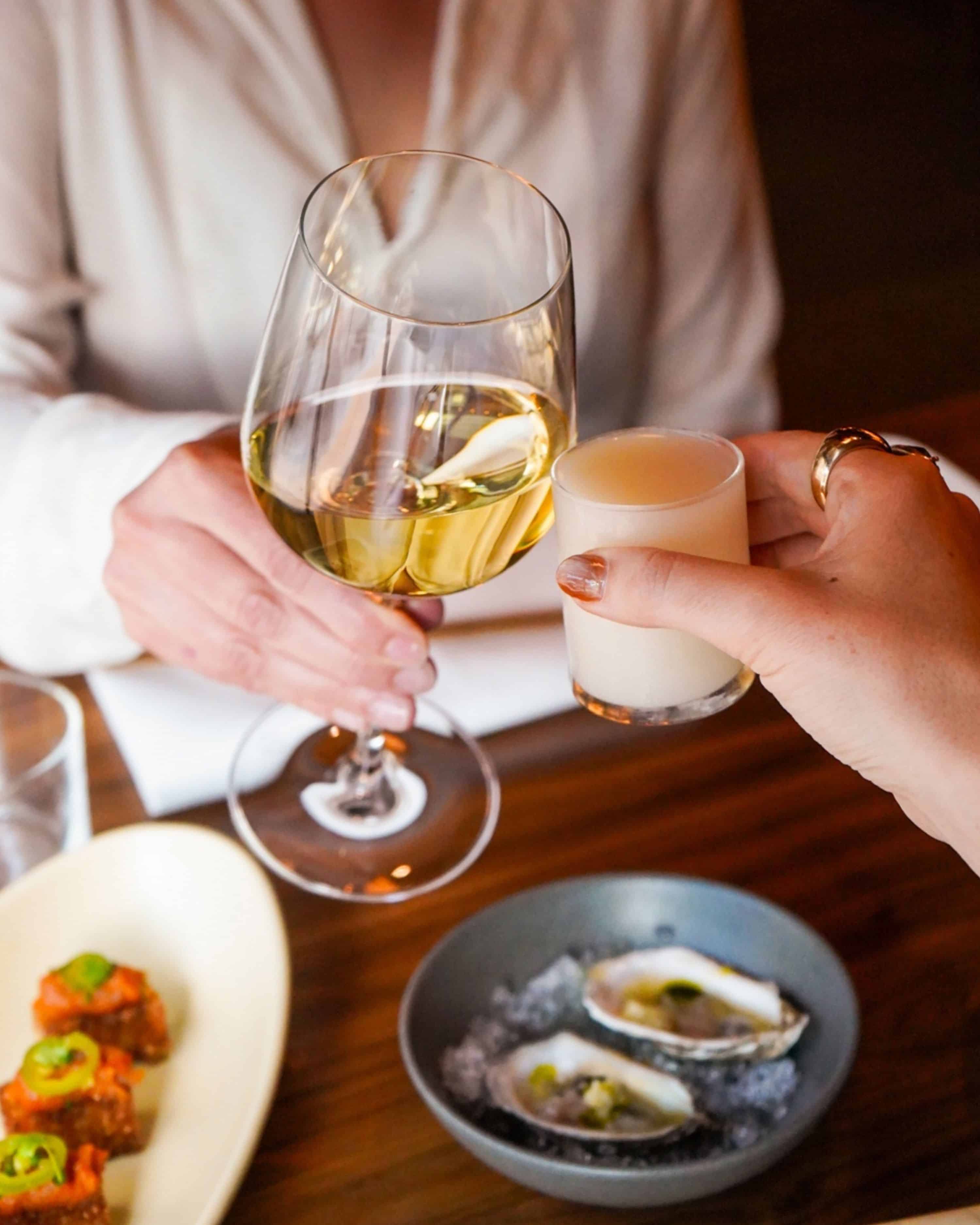 wine glass and sake glass cheersing over plated oysters